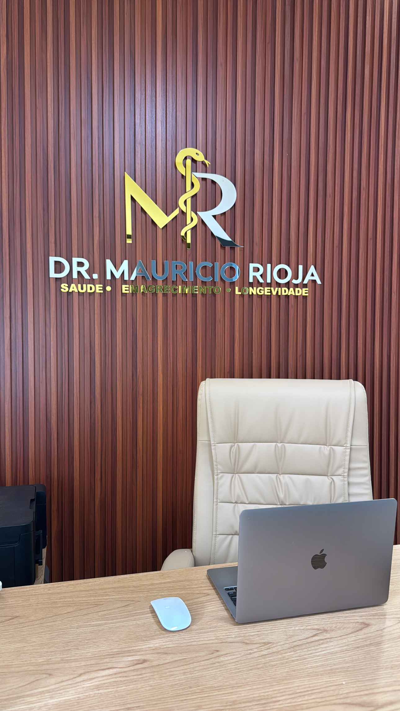 Consultório do Dr. Maurício Rioja, com identificação na parede e mesa de atendimento